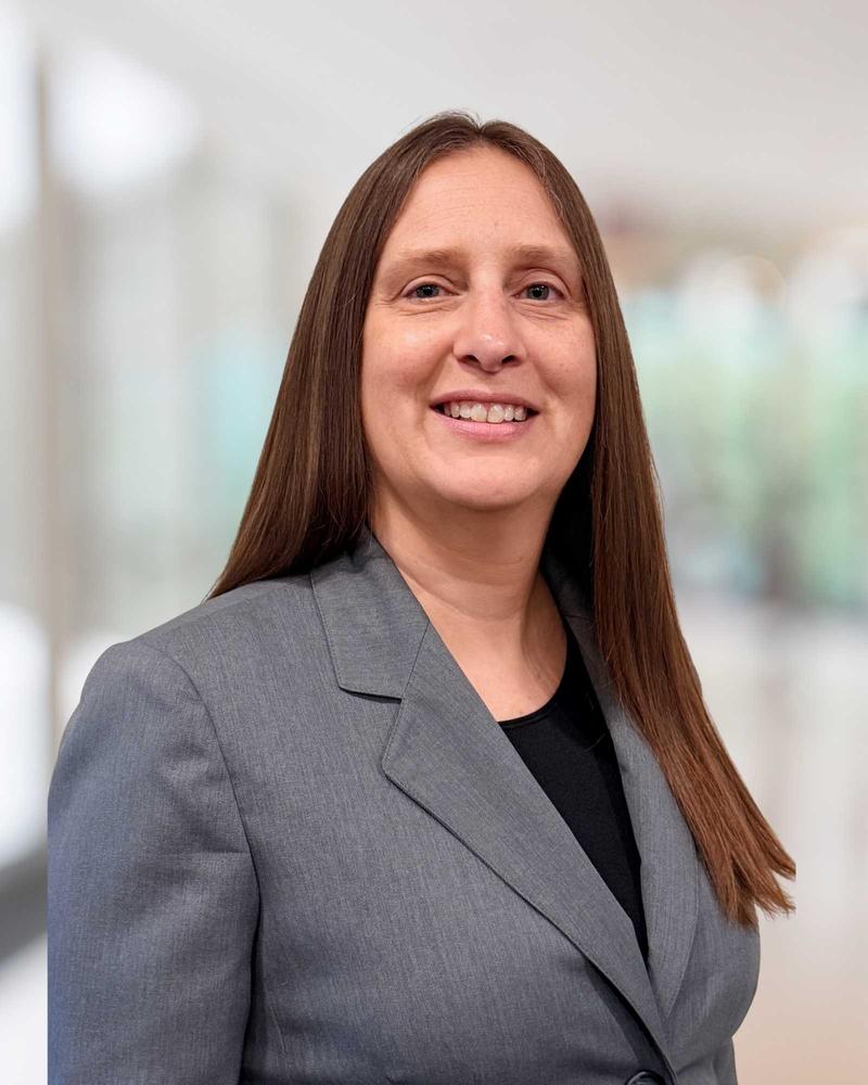 Michelle Hays, founder of CoreHR Solutions, smiling in a gray blazer and black top, with long straight brown hair, in a bright office